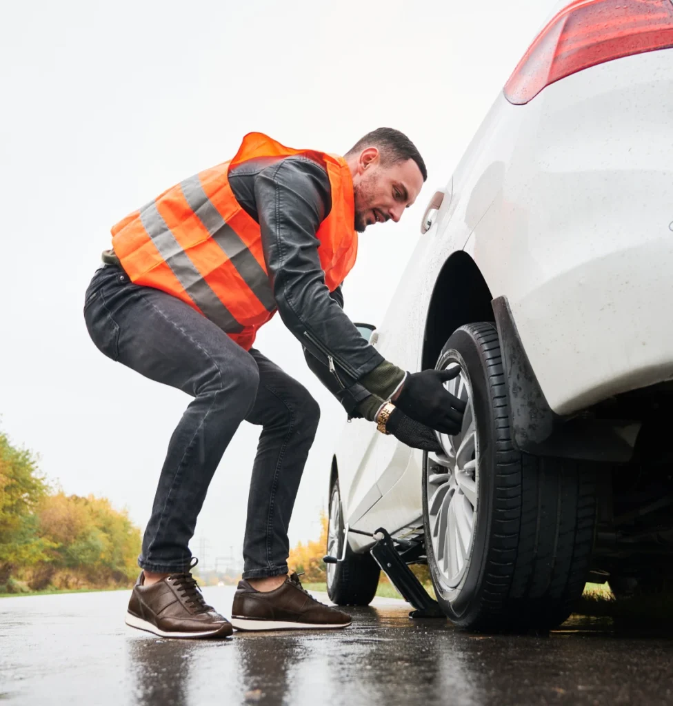 Roadside worker in a safety vest changing a car tire