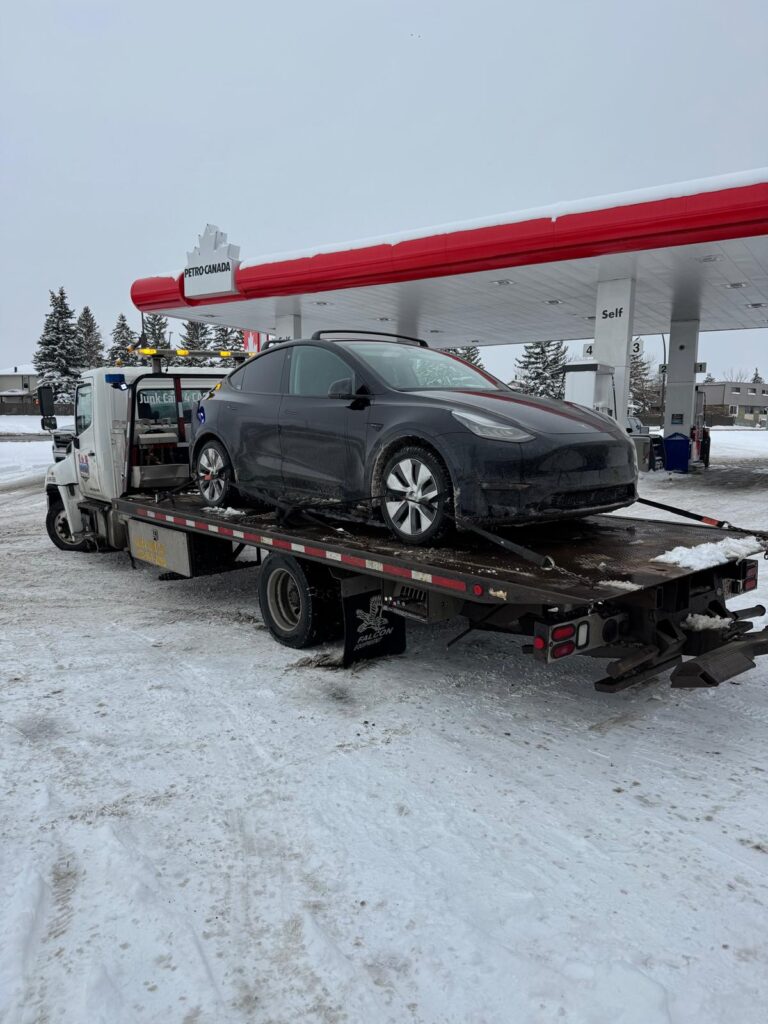 Tesla loaded on a flatbed tow truck at a gas station in winter