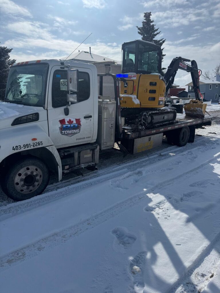 Mini excavator loaded on a BP Towing flatbed in winter