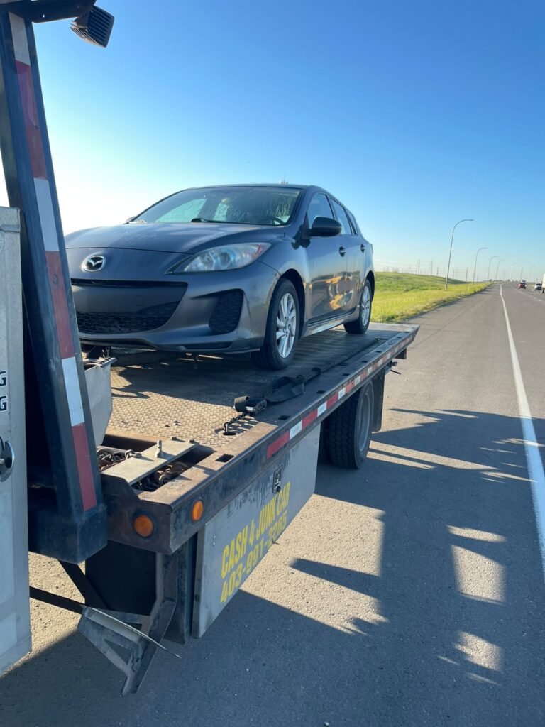 Grey Mazda hatchback loaded on a flatbed tow truck beside an Alberta highway